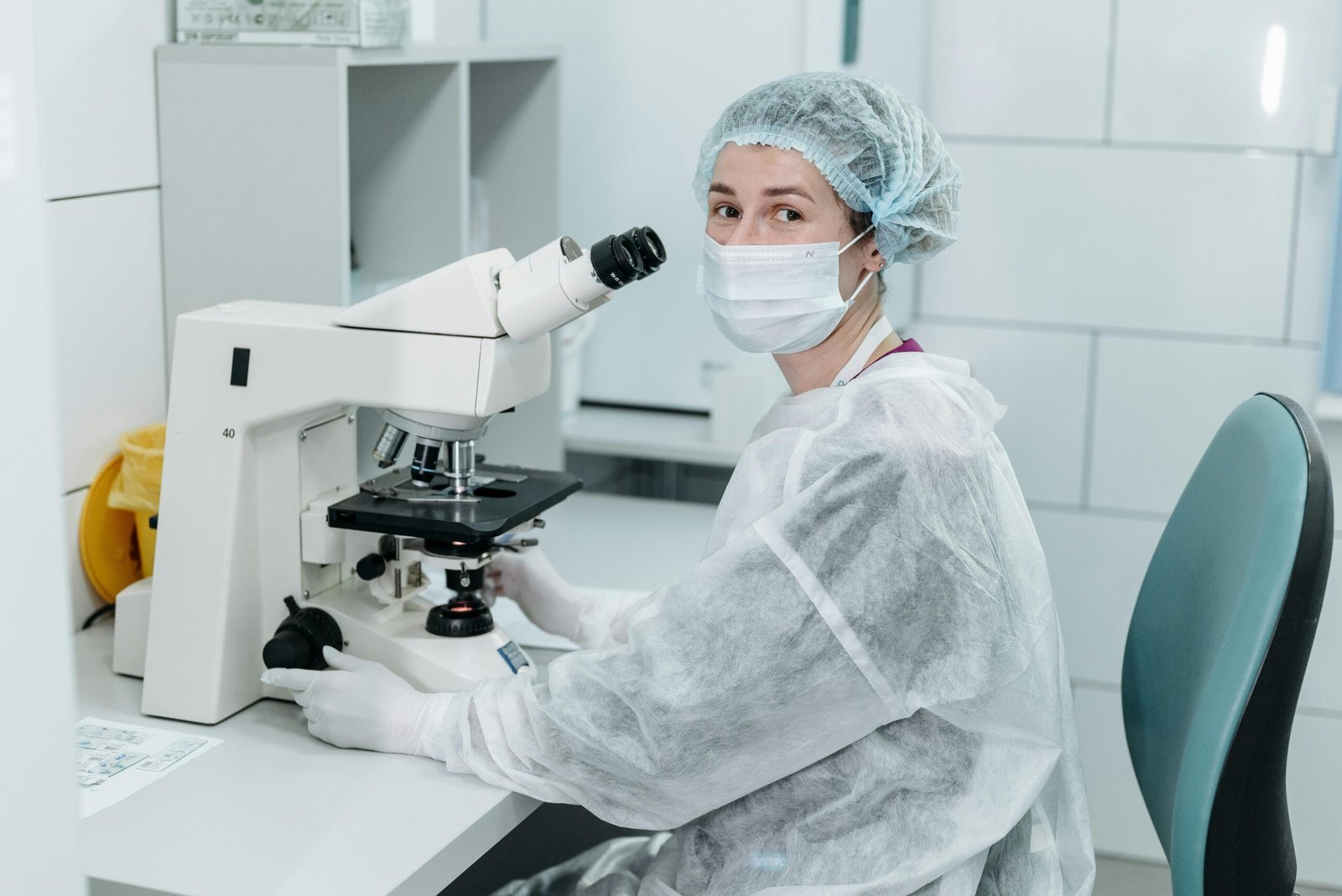 Scientist working with microscope in sterile lab environment, wearing protective gear and a mask.