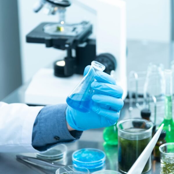 Scientist in gloves analyzing blue liquid in a laboratory setting with microscope and glassware.