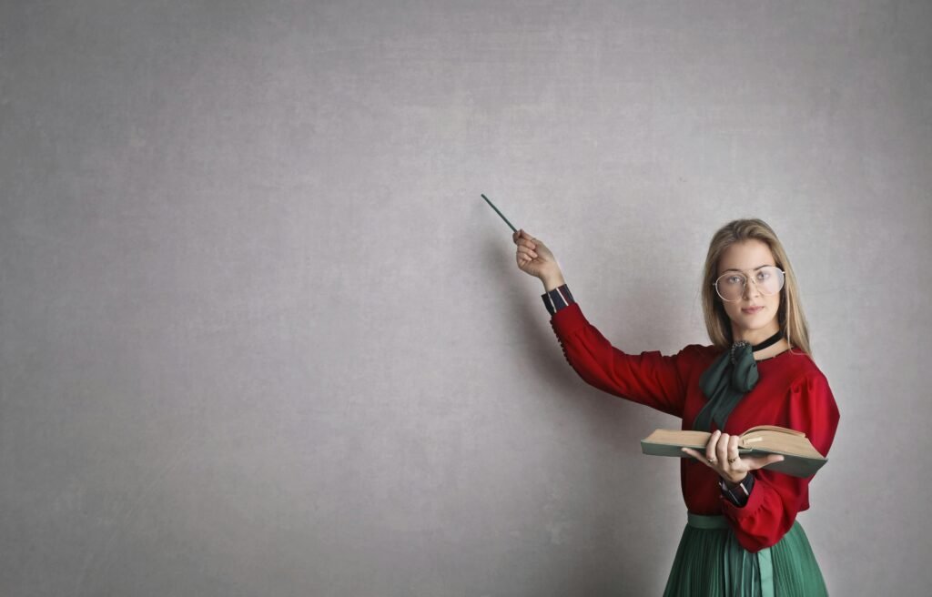 Female teacher pointing at a blank wall, holding a book, creating copyspace for educational content.