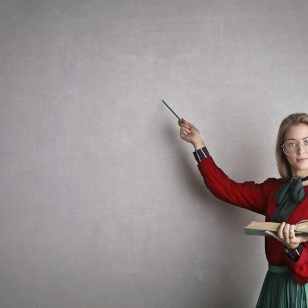 Female teacher pointing at a blank wall, holding a book, creating copyspace for educational content.