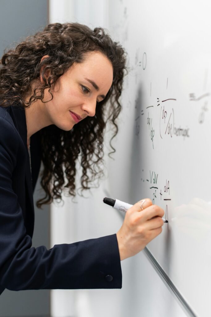 Female engineer solving equations on whiteboard with focus and precision.