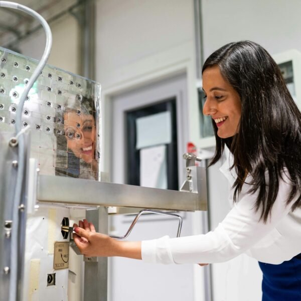 A female engineer operating machinery in a laboratory setting with a reflective surface.