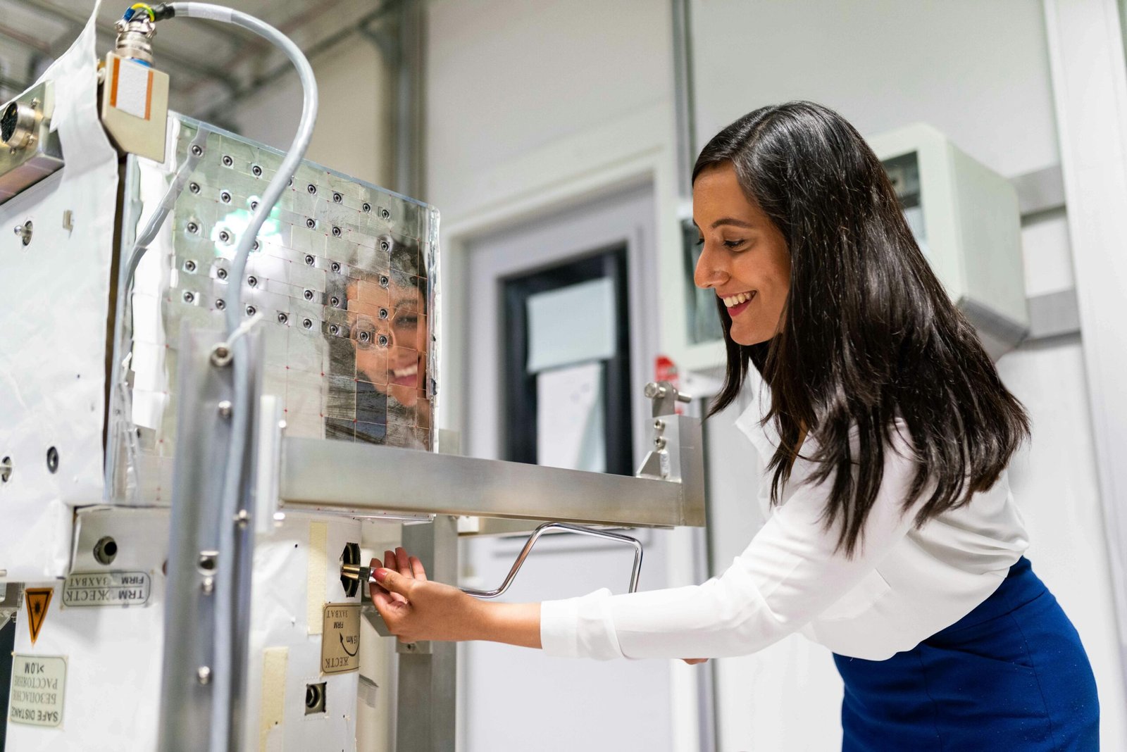 A female engineer operating machinery in a laboratory setting with a reflective surface.