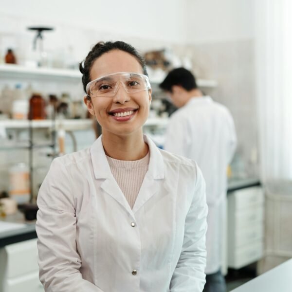 A confident female scientist in a lab coat smiling, working in an indoor laboratory environment.