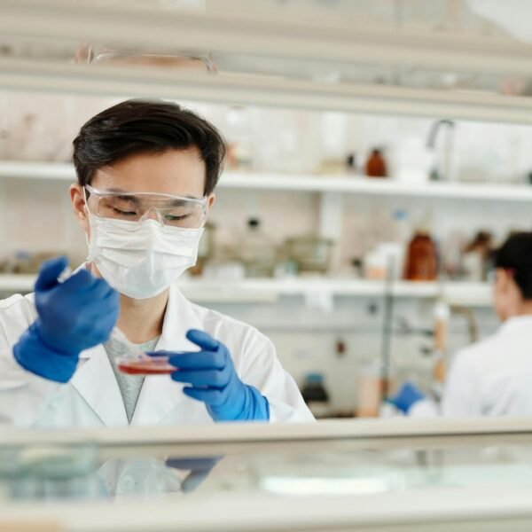 Researcher in a lab coat working on a scientific experiment with a petri dish and protective gear.