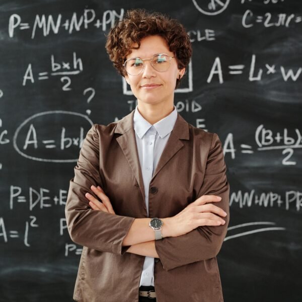 Confident female teacher standing with arms crossed in front of a detailed mathematical blackboard.