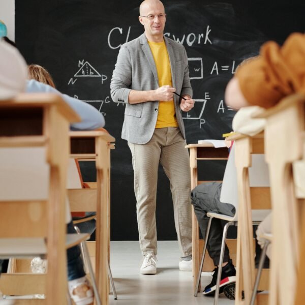 Bald teacher explaining geometry on blackboard to attentive students in classroom.