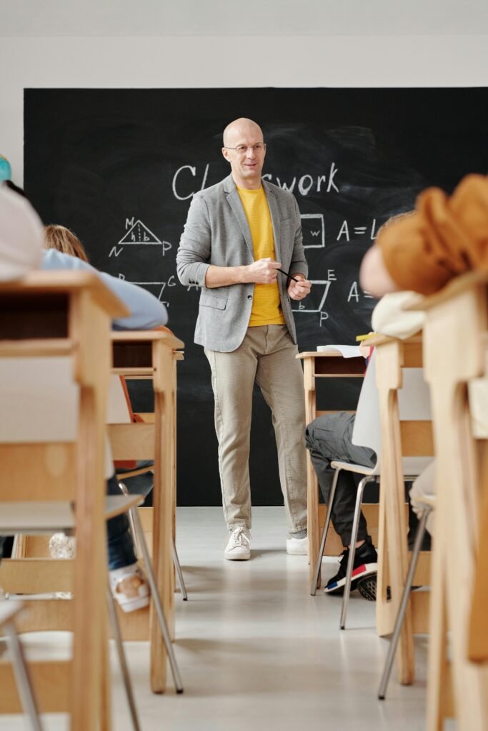 Bald teacher explaining geometry on blackboard to attentive students in classroom.