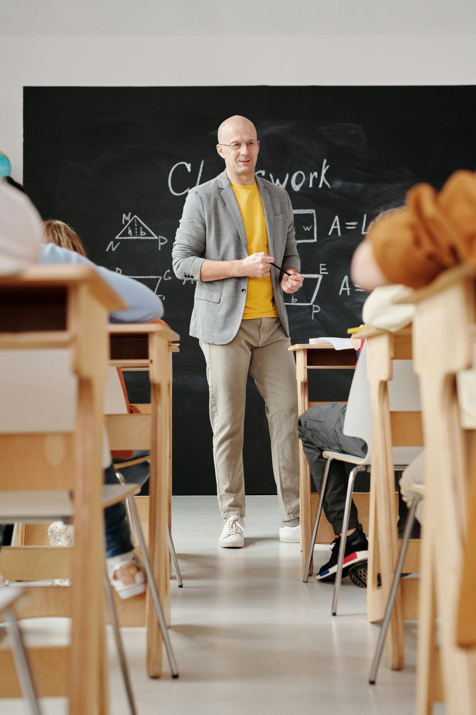 Bald teacher explaining geometry on blackboard to attentive students in classroom.