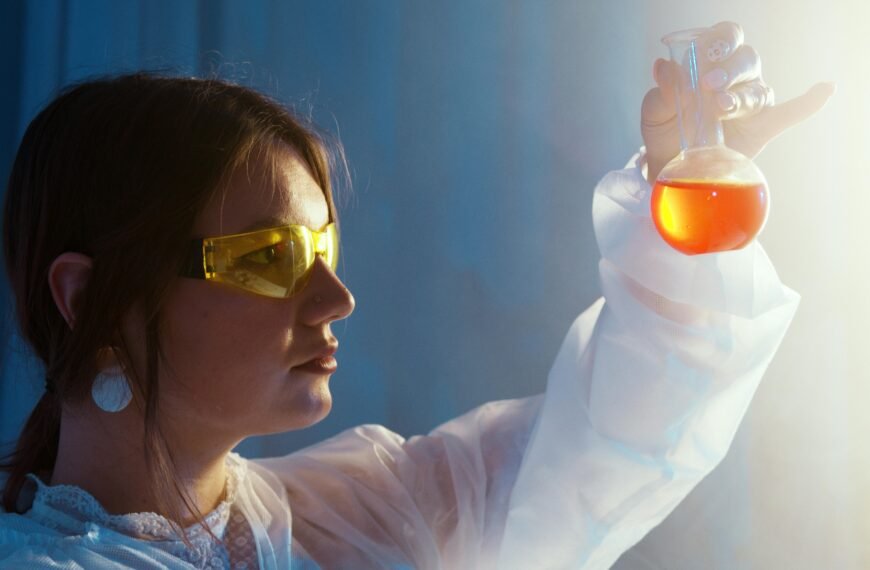 Woman in lab coat examining a vibrant liquid in a flask under lab lights.