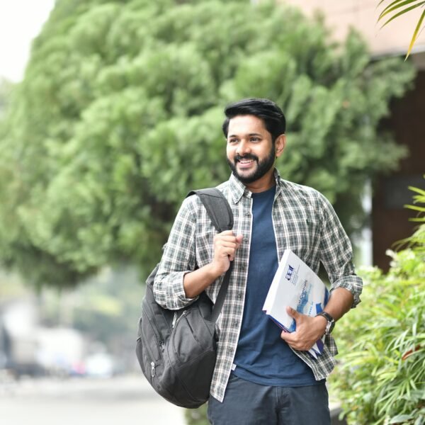 Young man smiling outdoors with backpack and books. Casual, candid, and vibrant student life moment.