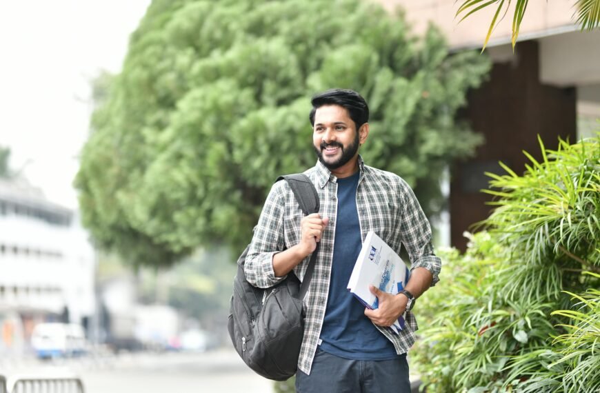 Young man smiling outdoors with backpack and books. Casual, candid, and vibrant student life moment.