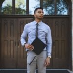 Young man in formal attire stands confidently with a graduation cap in hand.