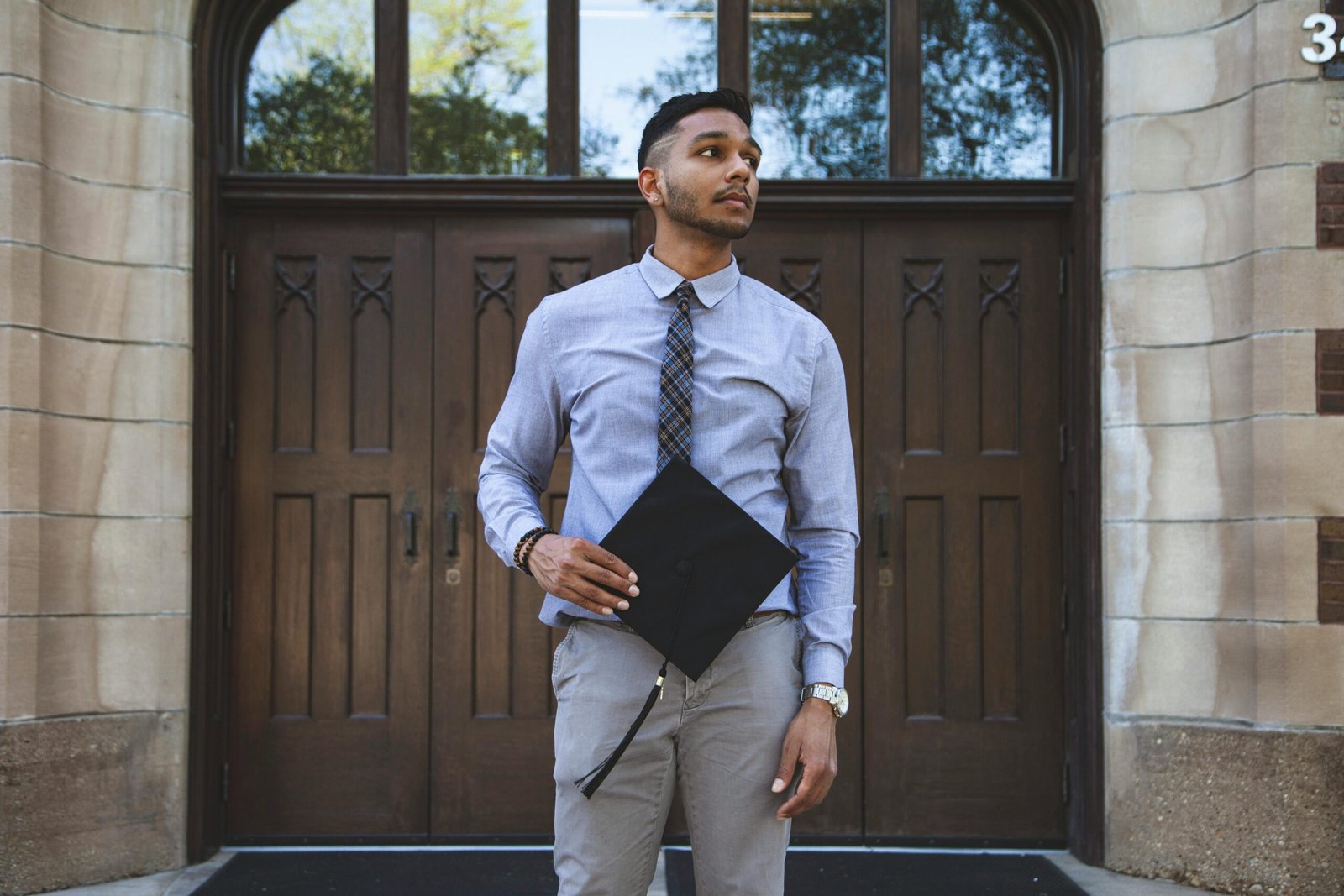 Young man in formal attire stands confidently with a graduation cap in hand.