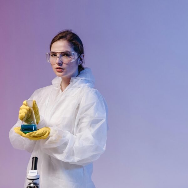 A woman scientist in lab gear analyzes a sample beside a microscope in a lab setting.