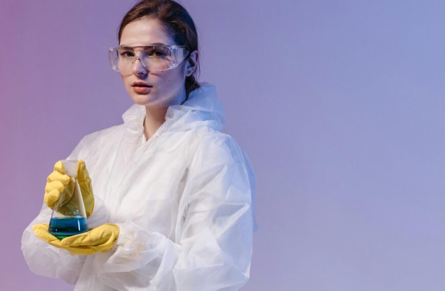 A woman scientist in lab gear analyzes a sample beside a microscope in a lab setting.