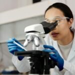 A female scientist examines samples using a microscope in a laboratory setting.