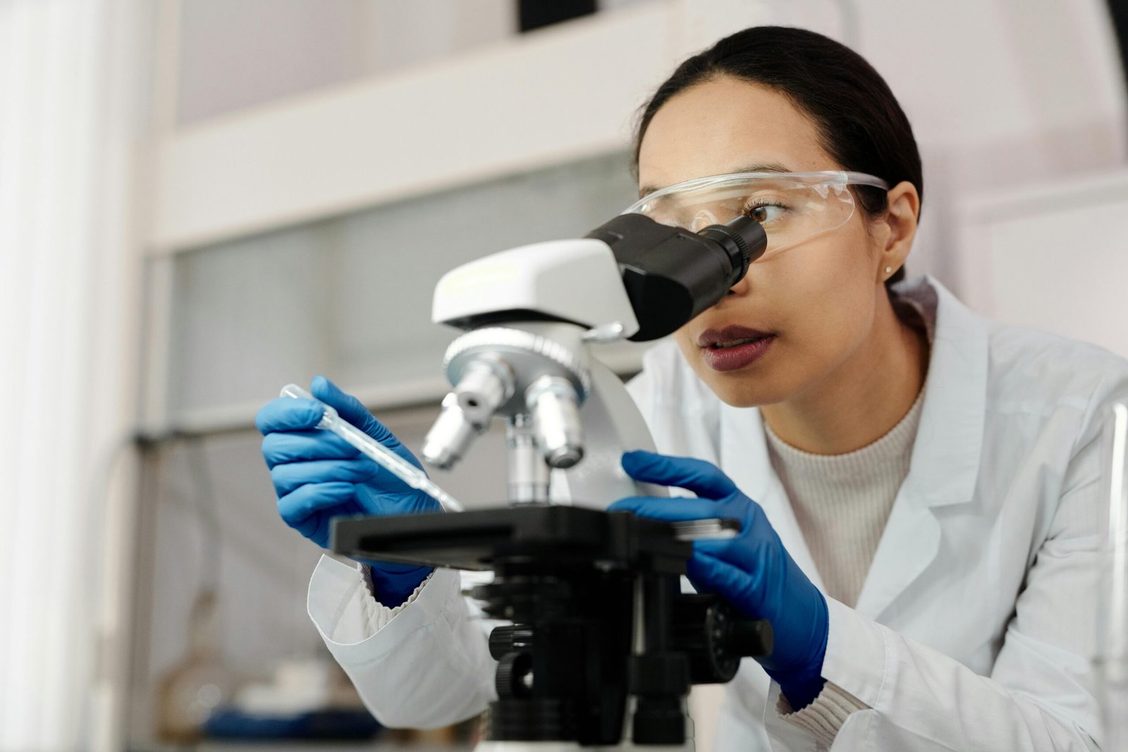 A female scientist examines samples using a microscope in a laboratory setting.